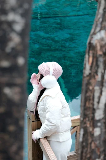 Woman in a white winter jacket beside a turquoise alpine lake
